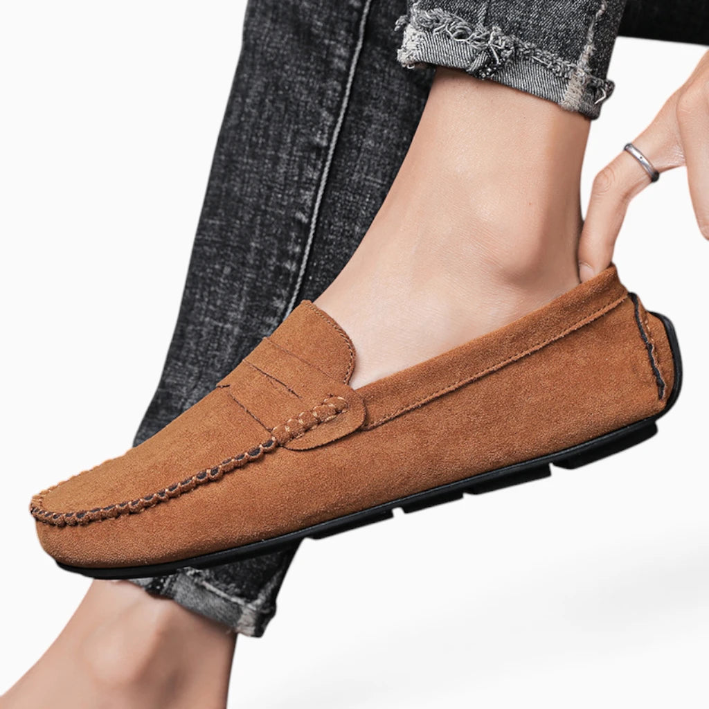 Mocassin daim homme porté, piqûres apparentes, semelle noire, vue de profil avec jambe